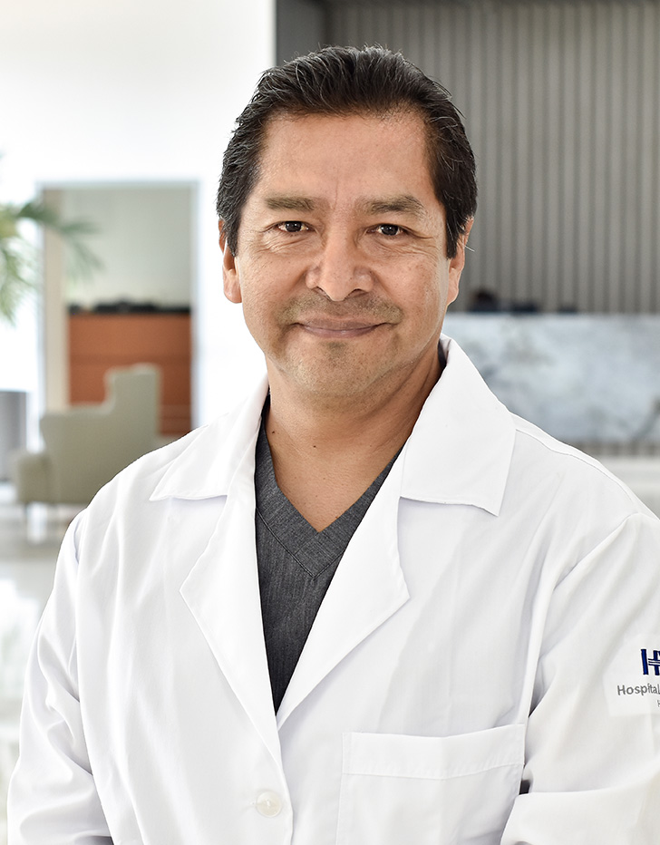 Es la foto de perfil de un urólogo en Tampico de Hospital Angeles Tampico. Usa una bata blanca con un uniforme médico negro. Tiene barba y cabello negro. Está serio.