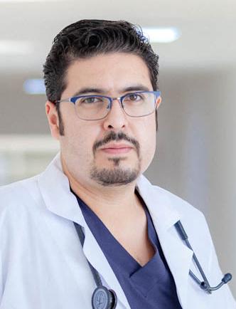 Es la foto de perfil de un geriatra en San Luis Potosí. Usa una bata blanca con un uniforme médico y un estetoscopio. Tiene el cabello y barba negra. Usa lentes y está serio.