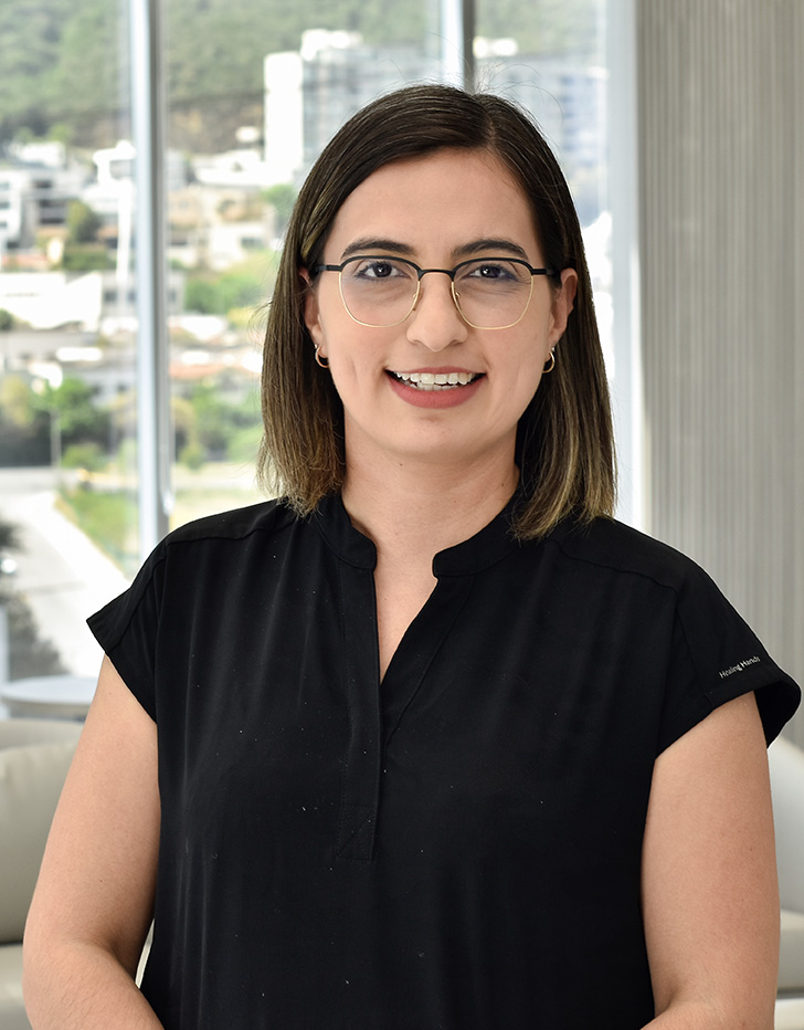 Es la foto de perfil de una médica especialista en medicina de rehabilitación en San Pedro Garza de Hospital Angeles Valle Oriente. Usa una blanca con un uniforme médico azul marino. Tiene el cabello largo y castaño. Usa un labial rojo.