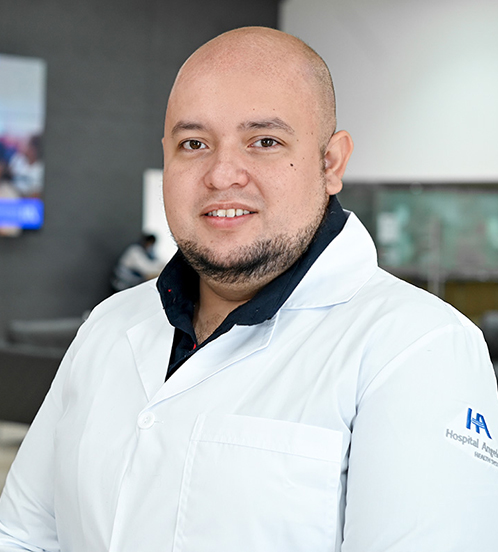 Es la foto de perfil de un ginecólogo y obstetra en San Luis Potosí de Hospital Angeles San Luis Potosí. Usa un uniforme médico azul. Es calvo y tiene la barba café oscuro. Está sonriendo ligeramente.