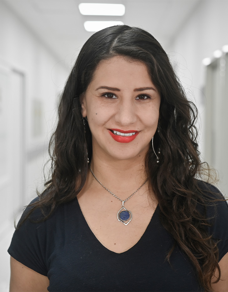 Es la foto de perfil de una cirujana de mano, microcirujana, ortopedista y traumatóloga en Ciudad de México de Hospital Angeles Universidad. Usa una blusa negra con un collar plata. Tiene el cabello largo, ondulado y negro. Está sonriendo y usa labial rojo.