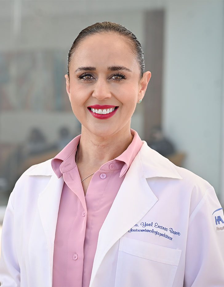 Es la foto de perfil de una endoscopista pediátrica, gastroenteróloga pediátrica y pediatra en Tijuana de Hospital Angeles Tijuana. Usa una bata blanca con una camisa rosa. Tiene el cabello castaño y rogido. Está sonriendo y usa labial rojo.