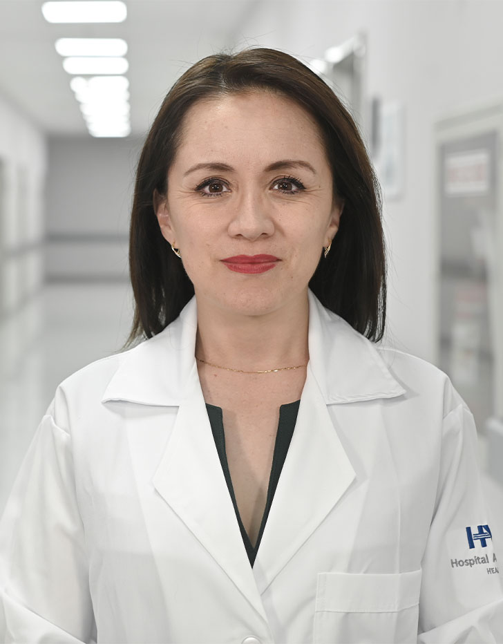 Es la foto de perfil de una ginecóloga y obstetra y cirujana oncóloga en Ciudad de México de Hospital Angeles Universidad. Usa una bata blanca. Tiene el cabello café oscuro y lacio. Usa un labial rojo. Está seria.