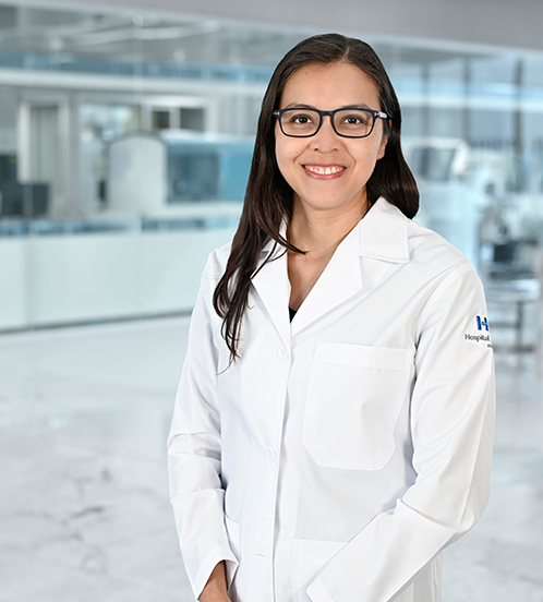 Es la foto de perfil de un cirujano neurológico en Guadalajara de Hospital Angeles Del Carmen. Utiliza una bata blanca y una blusa negra con detalles en blanco. La doctora usa lentes.