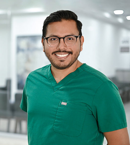Es la foto de perfil de un ginecólogo y obstetra en Ciudad de México de Hospital Angeles Acoxpa. Está usando un uniforme médico color verde. Tiene el cabello negro y sus lentes son cuadrados y negros.